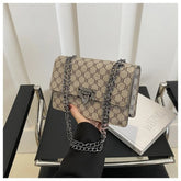 Beige handbag with black chain strap held by a person on a black chair.
