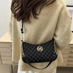 Person wearing a beige sweater with a black patterned handbag featuring a gold logo.
