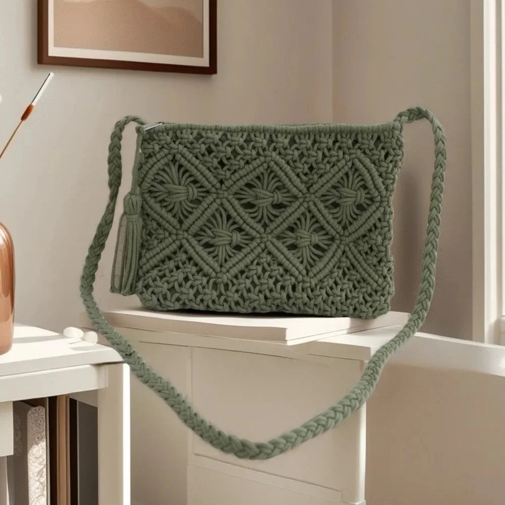 A sage green macrame shoulder bag with a woven geometric pattern and a braided strap, styled on a white table in a bright room.