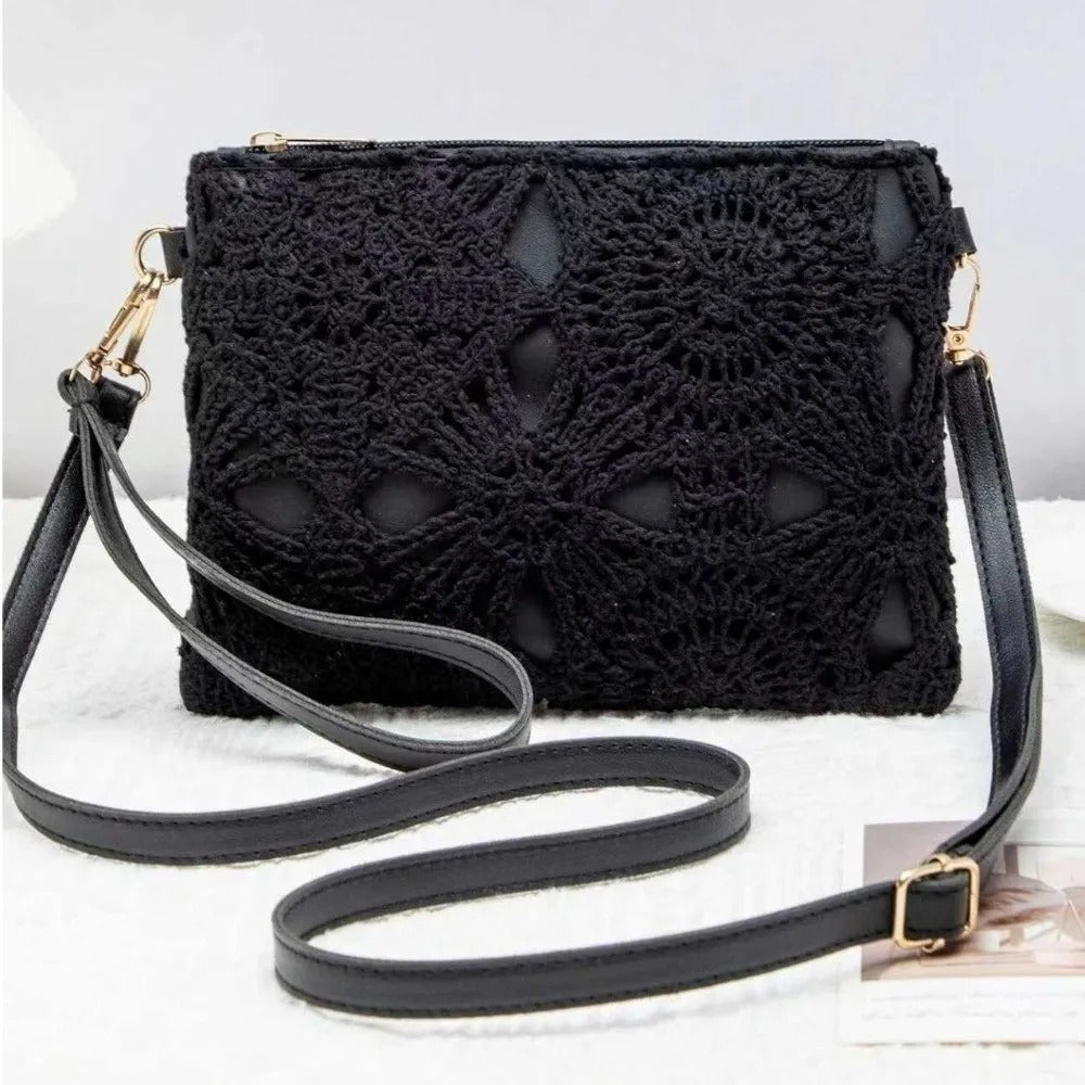 Black crocheted clutch handbag with a long shoulder strap and gold-tone hardware, displayed on a light textured surface.