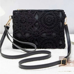 Black crocheted clutch handbag with a long shoulder strap and gold-tone hardware, displayed on a light textured surface.