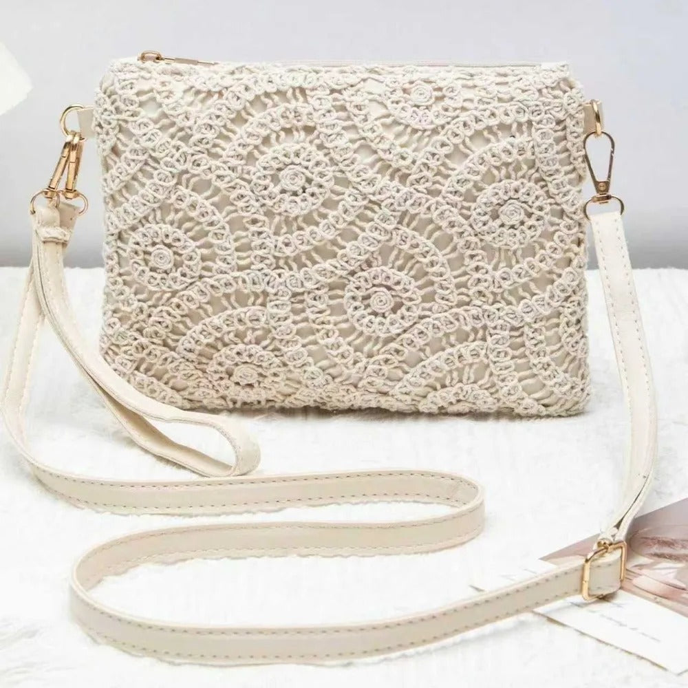 An off-white crocheted lace clutch bag with a matching faux-leather shoulder strap and gold-tone hardware, displayed on a white textured surface.