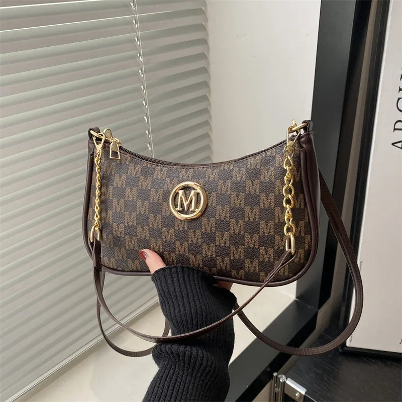 Brown handbag with gold chain detail held by a person wearing a black sweater.
