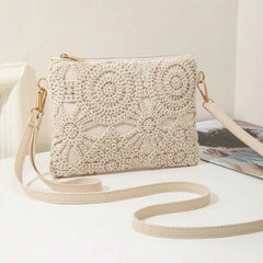 A cream-colored crocheted clutch bag with a matching shoulder strap and gold-tone hardware, displayed on a white surface next to a magazine.
