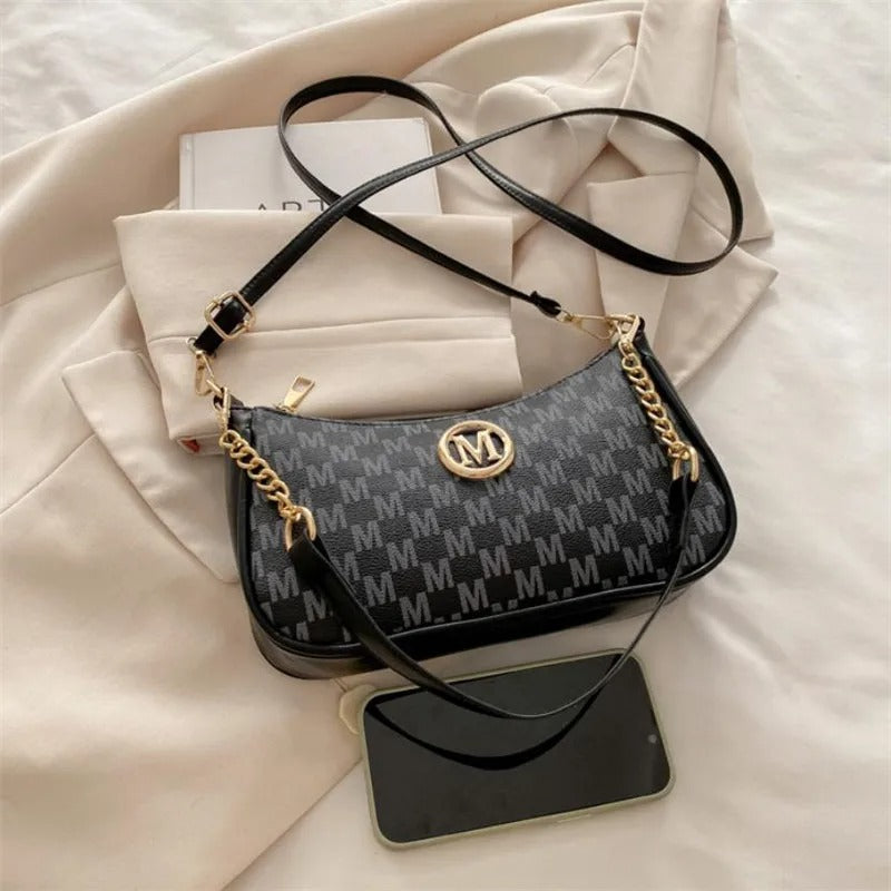 Black handbag with gold chain detail on a light beige fabric background