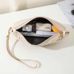 A beige crocheted wristlet clutch bag with a matching wrist strap, shown open on a white tabletop with a laptop and camera inside.