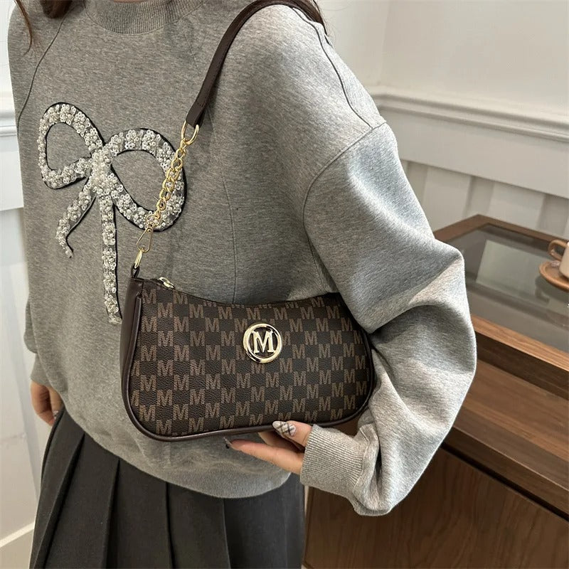Person wearing a gray sweatshirt with a large bow design, holding a patterned handbag.