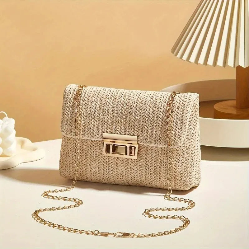 Beige woven handbag with a gold chain on a beige surface with a lamp in the background