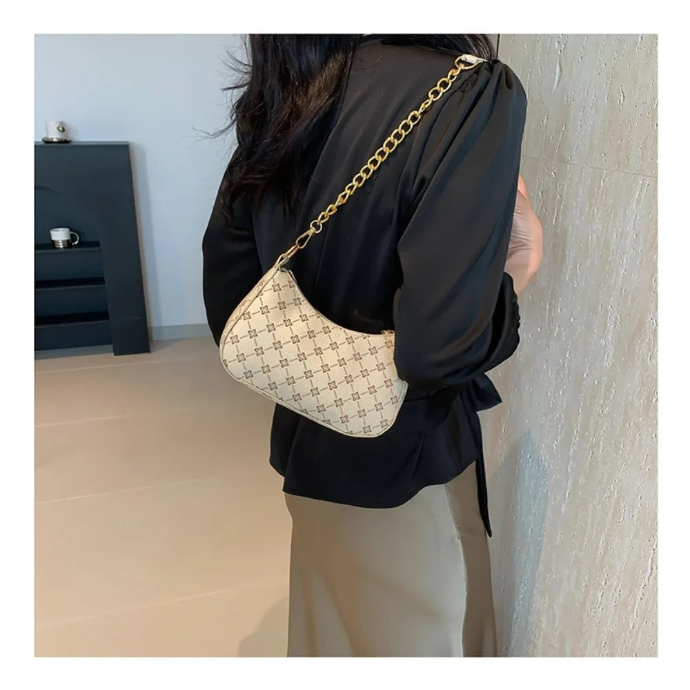 Person wearing a black outfit with a beige handbag featuring a gold chain strap.