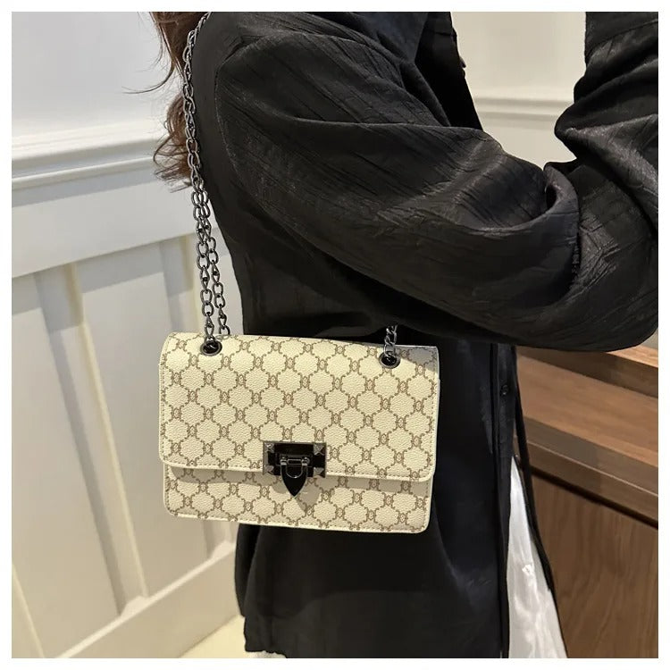 Person holding a patterned handbag with a chain strap indoors.