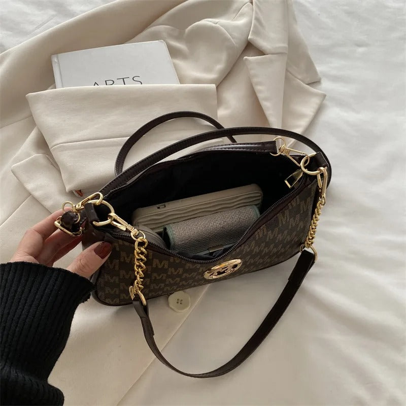 Brown handbag with gold chain detail held by a hand on a white surface
