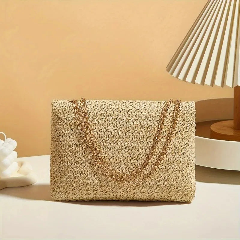 Woven handbag with gold chain on a beige surface with a lamp in the background