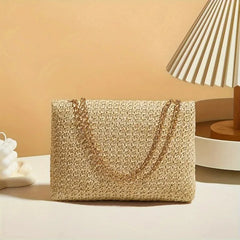 Woven handbag with gold chain on a beige surface with a lamp in the background