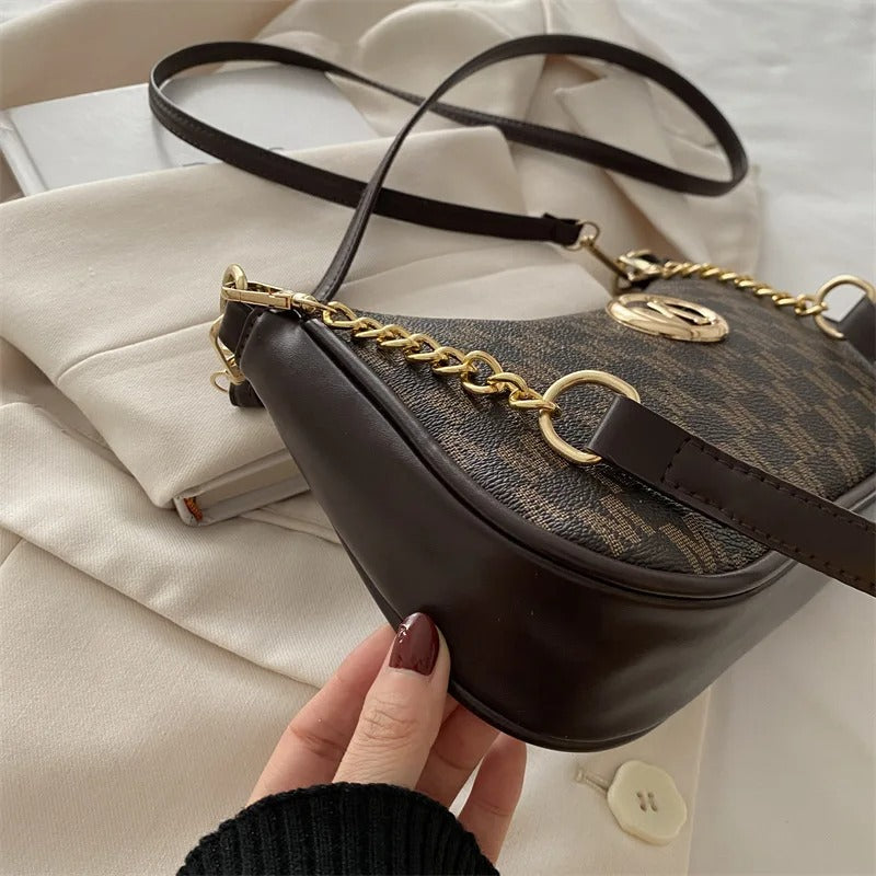 Brown handbag with gold chain detail held by a hand on a light background