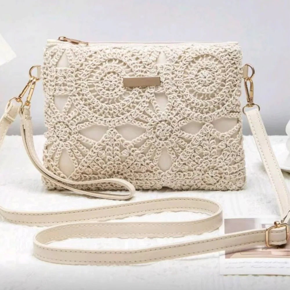 An off-white crocheted clutch bag with a matching shoulder strap, displayed on a white textured surface with a neutral background.