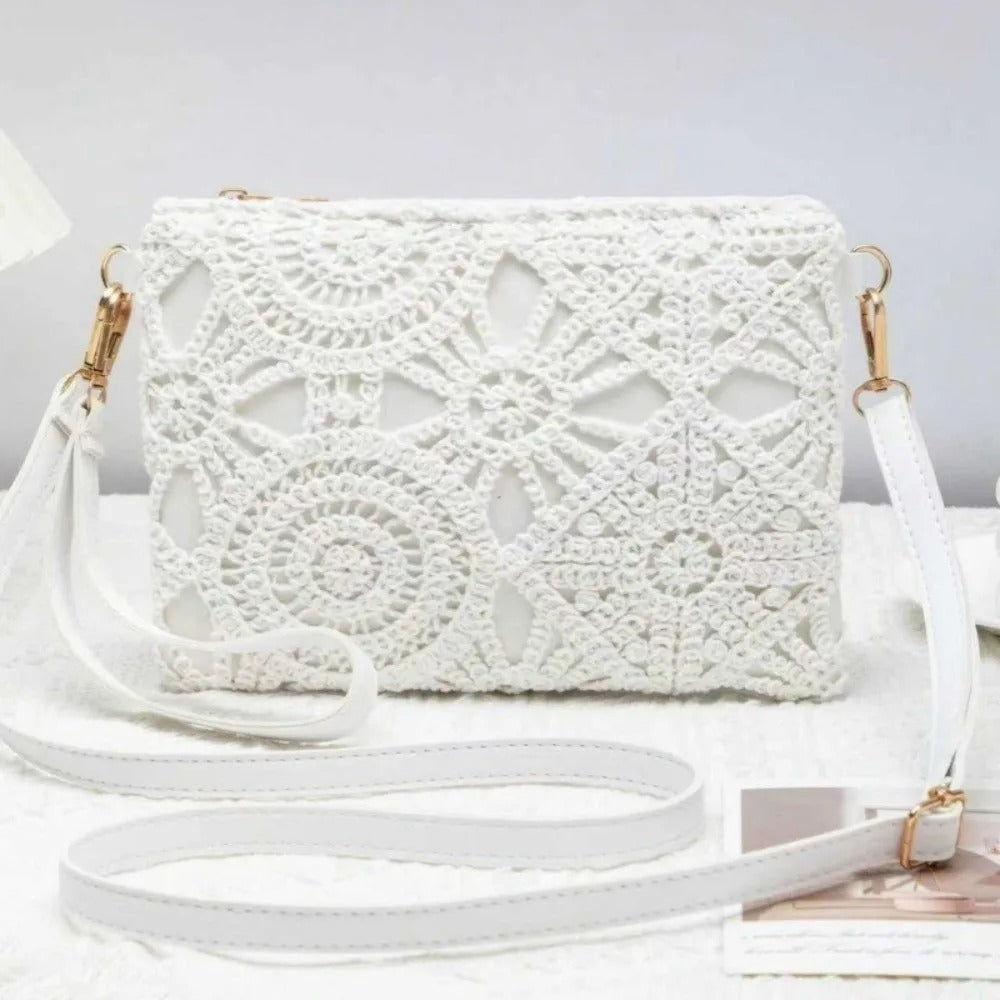 White crocheted clutch handbag with gold-tone hardware and a long white shoulder strap, displayed on a light surface against a soft white background.