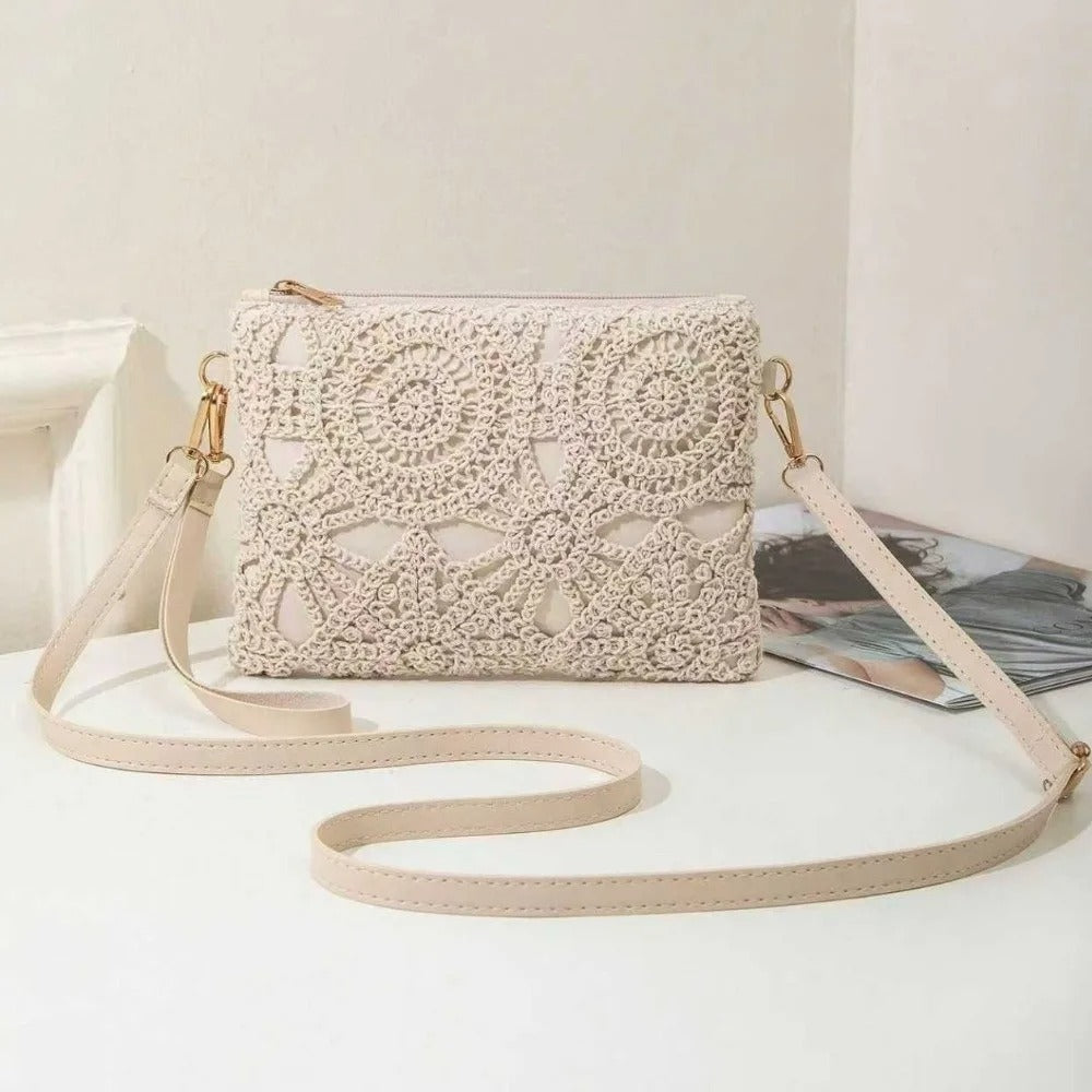 A beige crocheted clutch bag with a matching faux-leather shoulder strap and gold-tone hardware, displayed on a white surface with a magazine in the background.